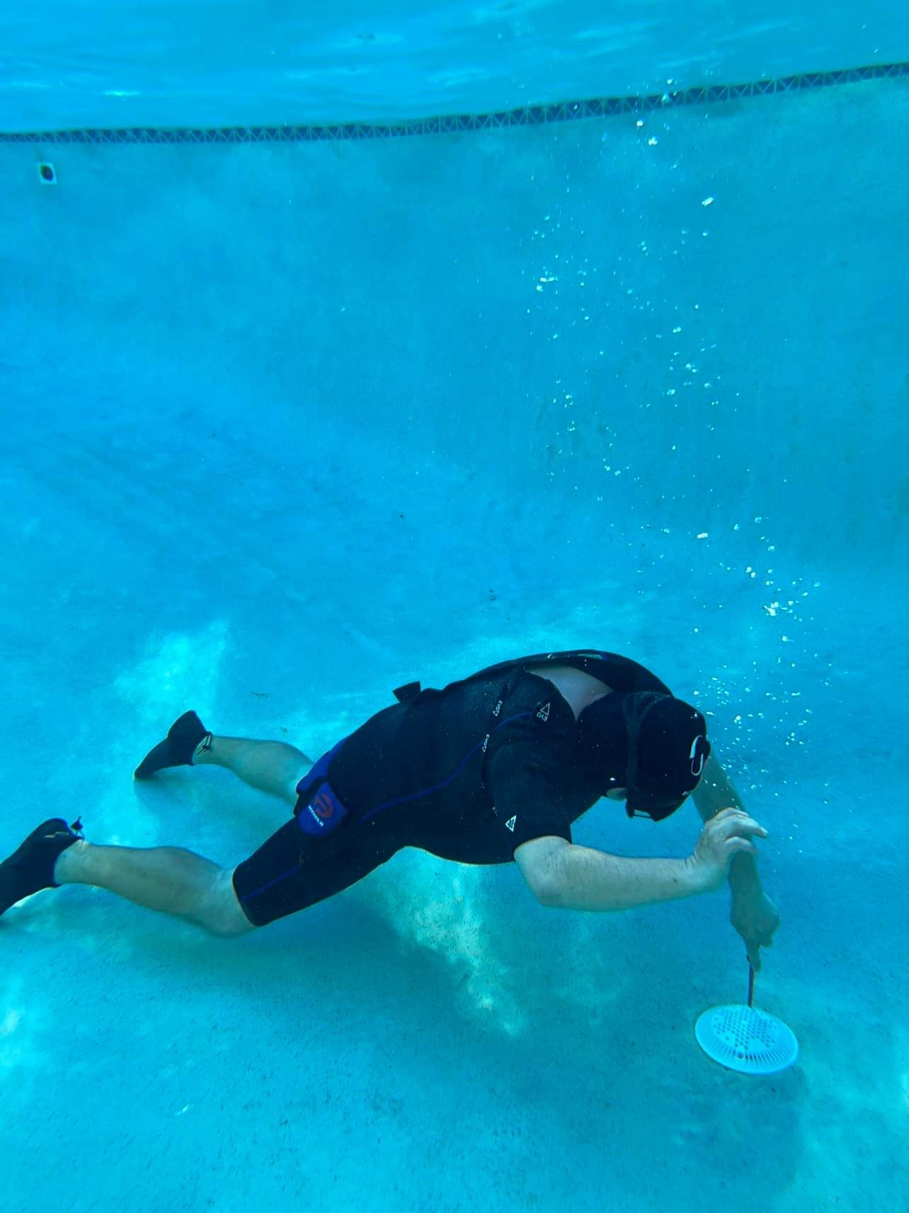 Technician underwater working with a tool beside a pool drain cover